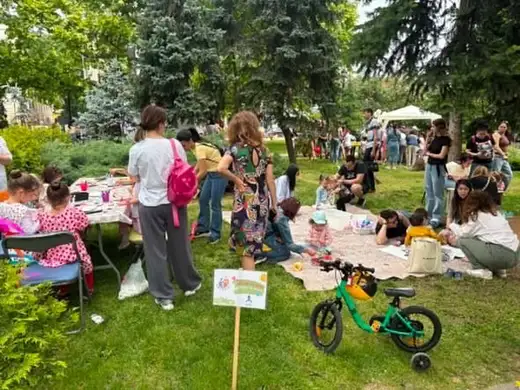 Общ изглед от фестивала в парка — маси с материали, деца върху одеяла и детско колело на тревата.