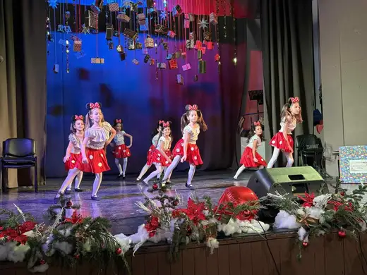 Момичета в народни носии танцуват на сцената.