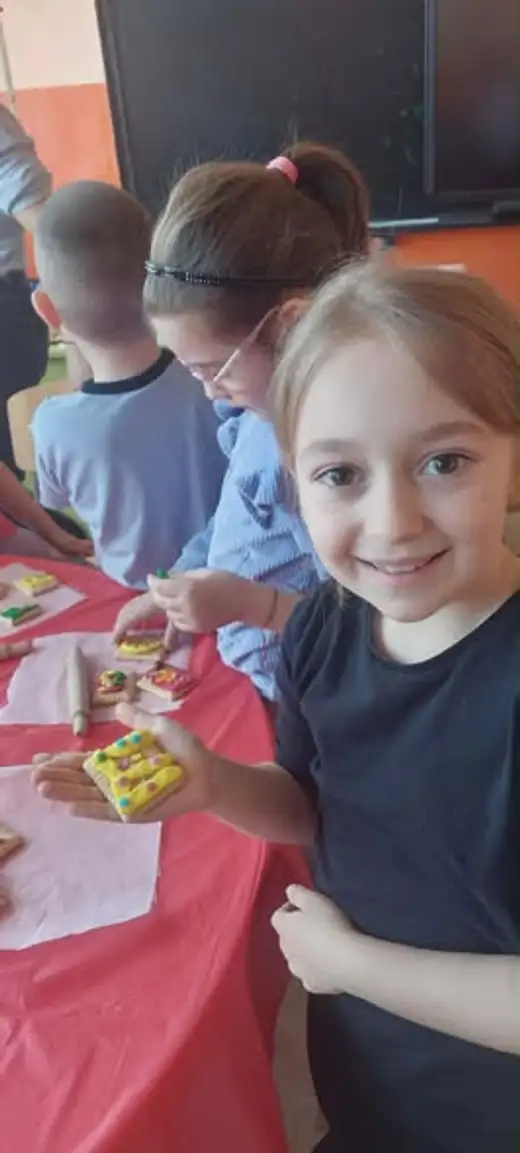 Момиче показва бисквитка, украсена с жълт фондан, а до нея друго дете украсява своята.