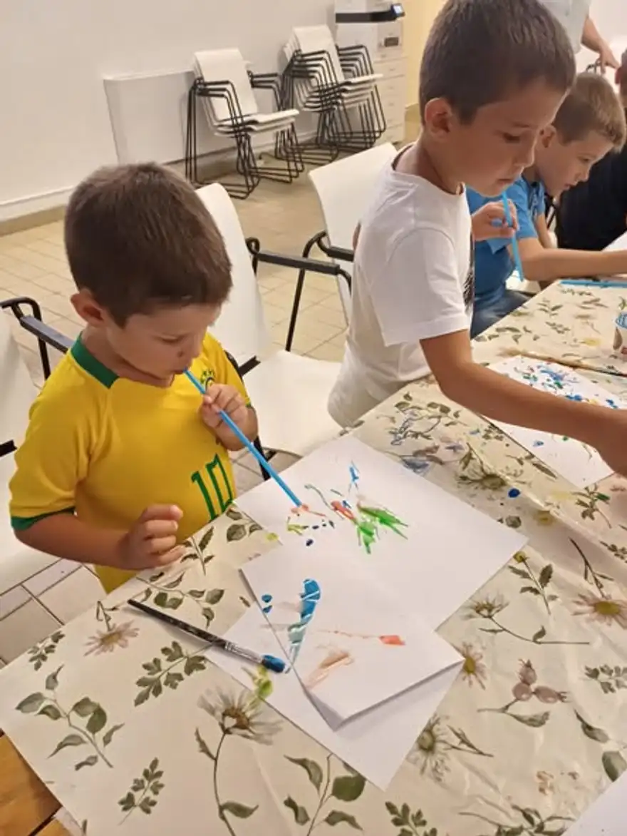 Момче рисува с четка и синя боя на дълга маса.