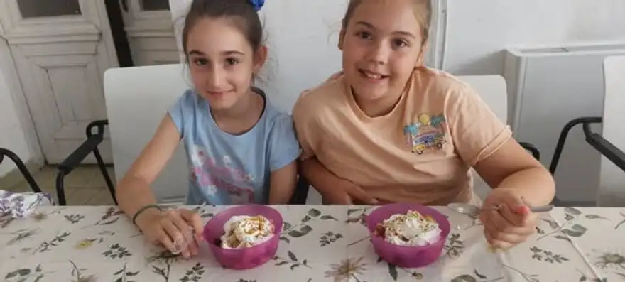 Две момичета се усмихват над чашки с плодова салата и сметана.