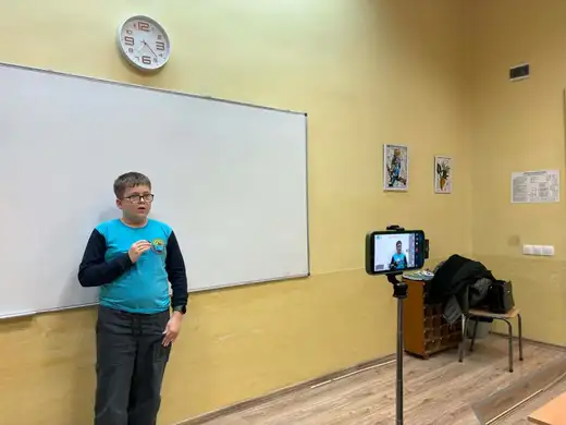 Ученик говори пред класната стая до телефон на статив.