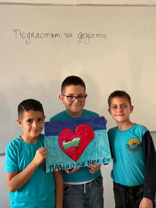 Трима ученици държат плакат с червено сърце.
