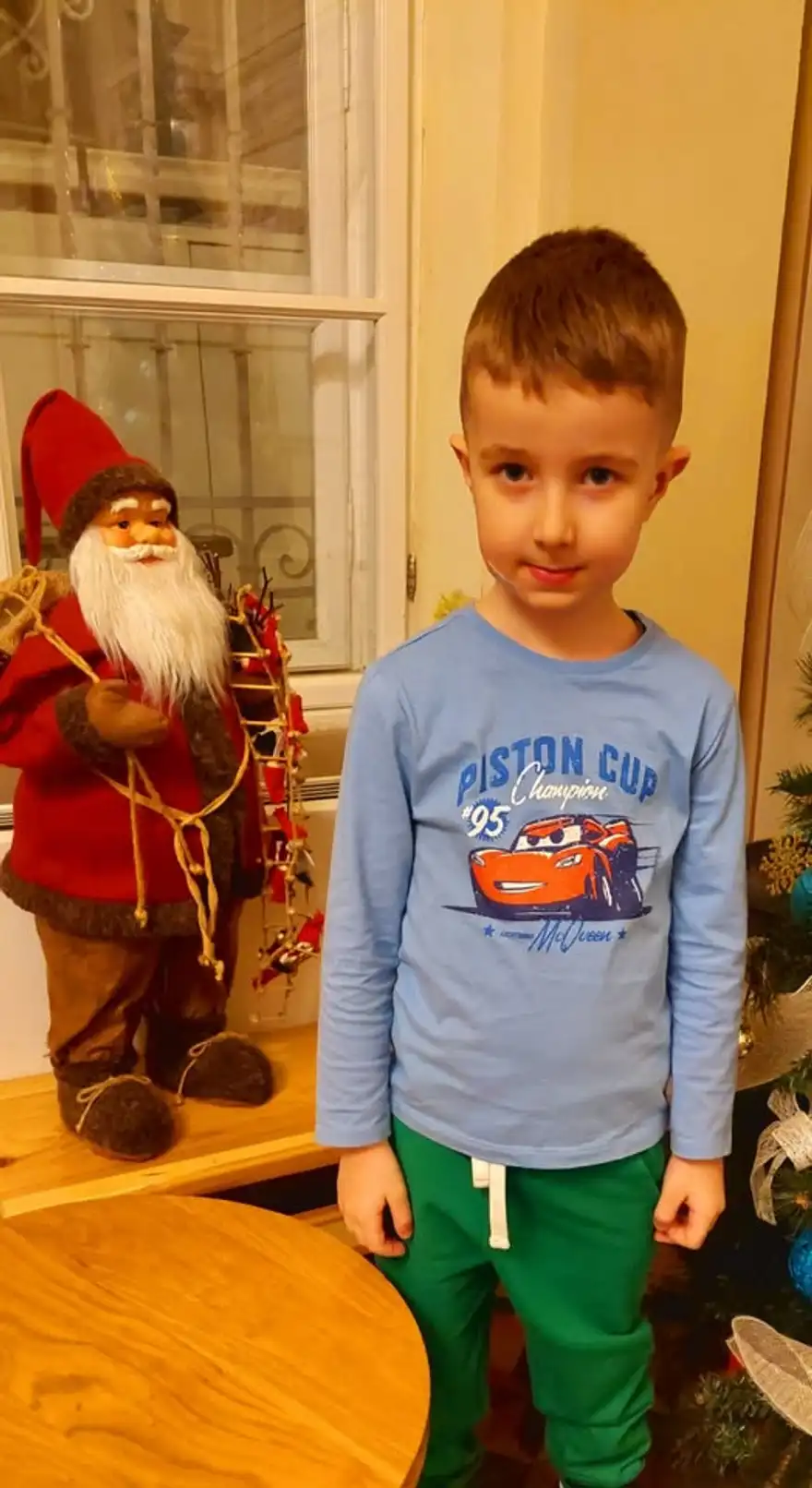 Момче стои до кръгла маса с фигура на Дядо Коледа върху нея.